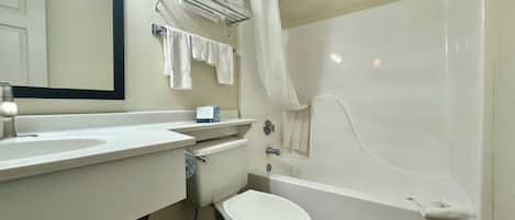 Un baño con inodoro, lavabo y bañera. Hay un perchero con toallas y una cortina de ducha.