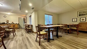 A spacious dining area with wooden tables and chairs, a kitchen in the background, and a large window providing natural light. - Quality Inn & Suites Alexandria (Alexandria)