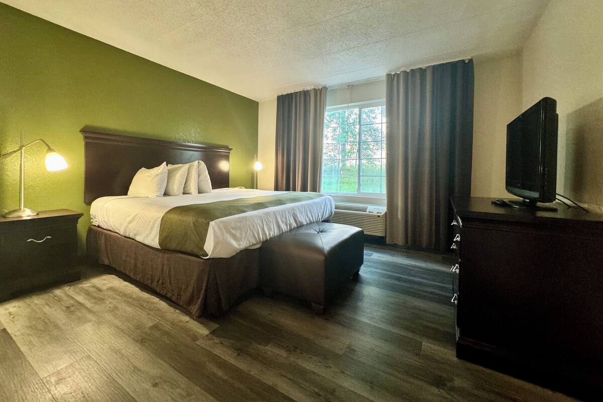 A hotel room with a bed, bedside lamp, TV, and a window with curtains.