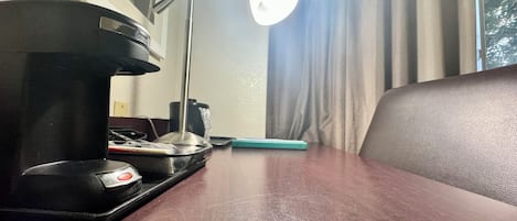 Un escritorio de madera con una cafetera, una lámpara y un teléfono inteligente.