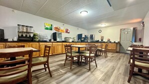 A restaurant with wooden tables and chairs, a kitchen area with appliances, and a clock on the wall.