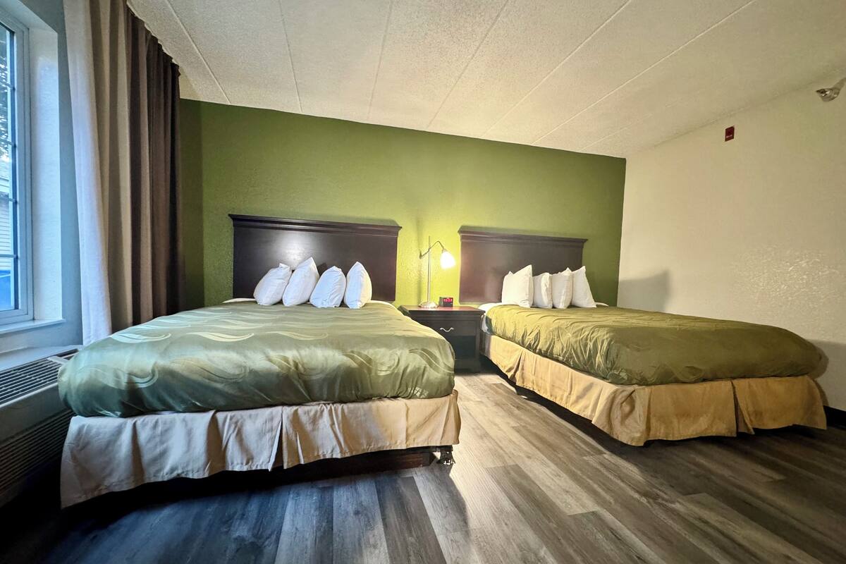 A hotel room with two beds, green walls, wooden flooring, and a window with curtains.