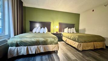 Habitación de hotel con dos camas, paredes verdes, suelo de madera y una ventana con cortinas.