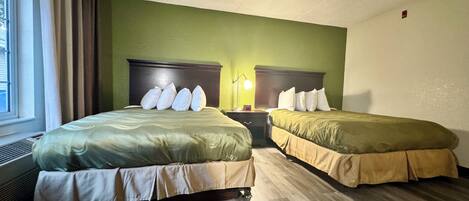 Habitación de hotel con dos camas, paredes verdes, suelo de madera y una ventana con cortinas.