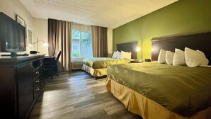 A hotel room with two beds, a desk with a chair, a television, and a window with curtains.