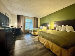 A hotel room with two beds, a desk with a chair, a television, and a window with curtains.