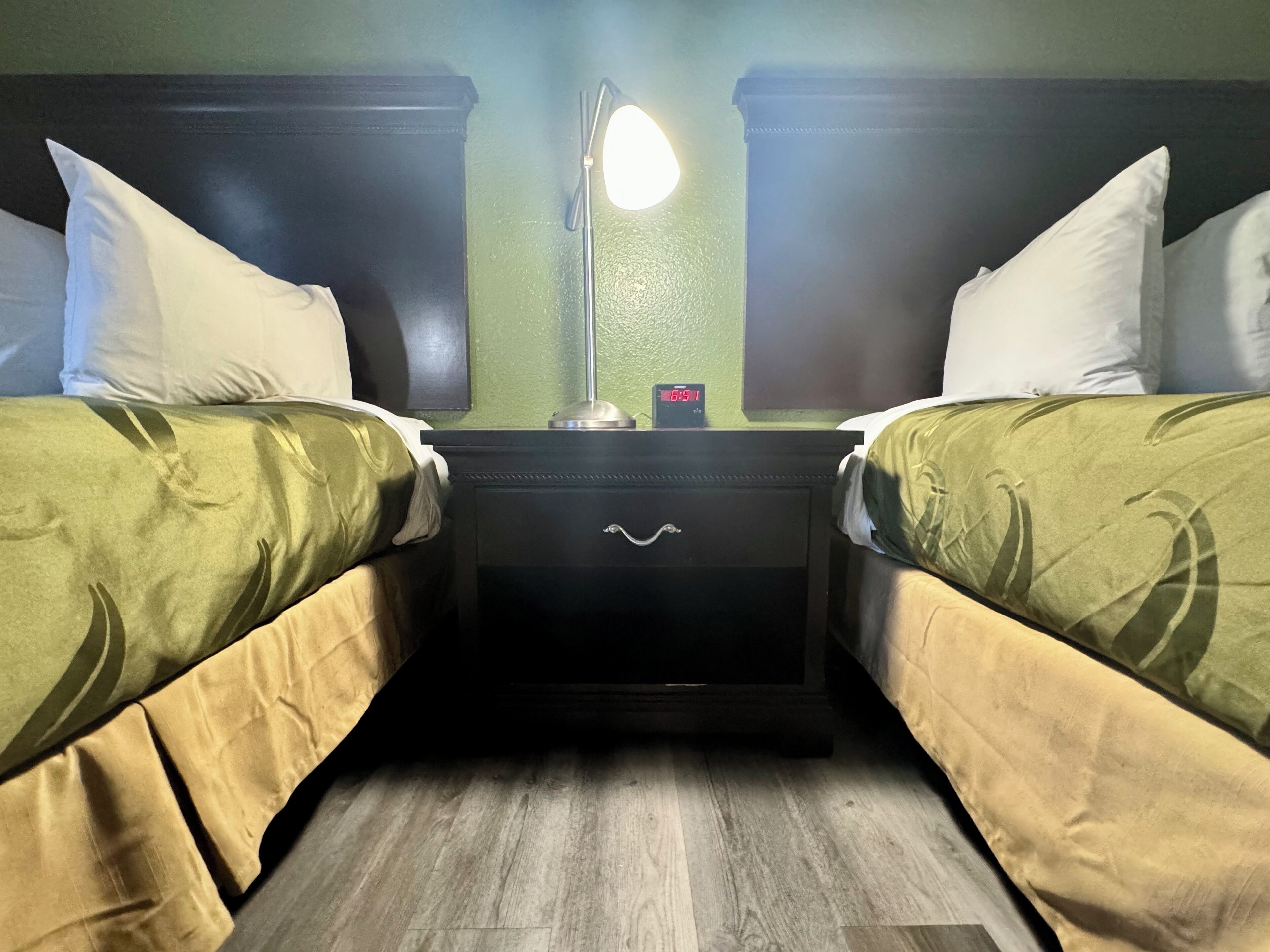 A room with two beds, a nightstand with a lamp, and a clock displaying 6:51.