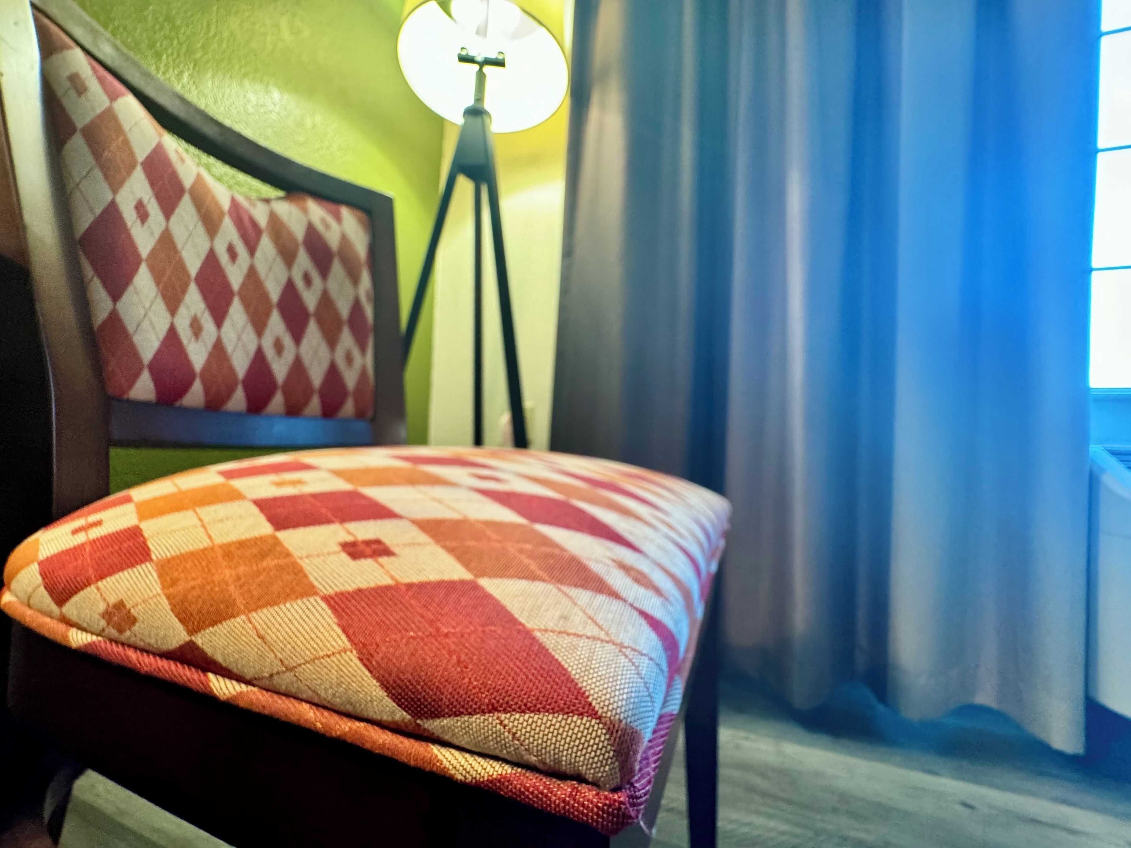A bed with a checkered pillow, a lamp, and curtains.