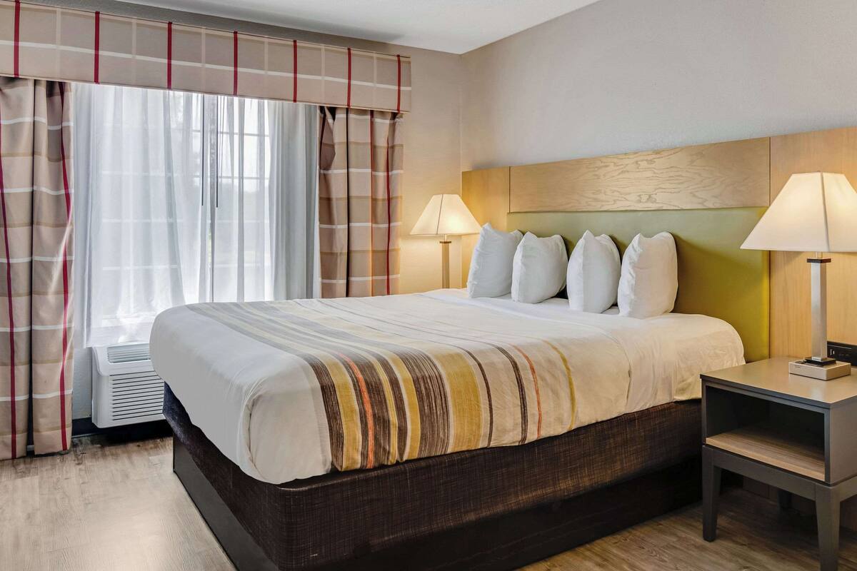 A hotel room with a large bed, two bedside lamps, a headboard, and a window with curtains.