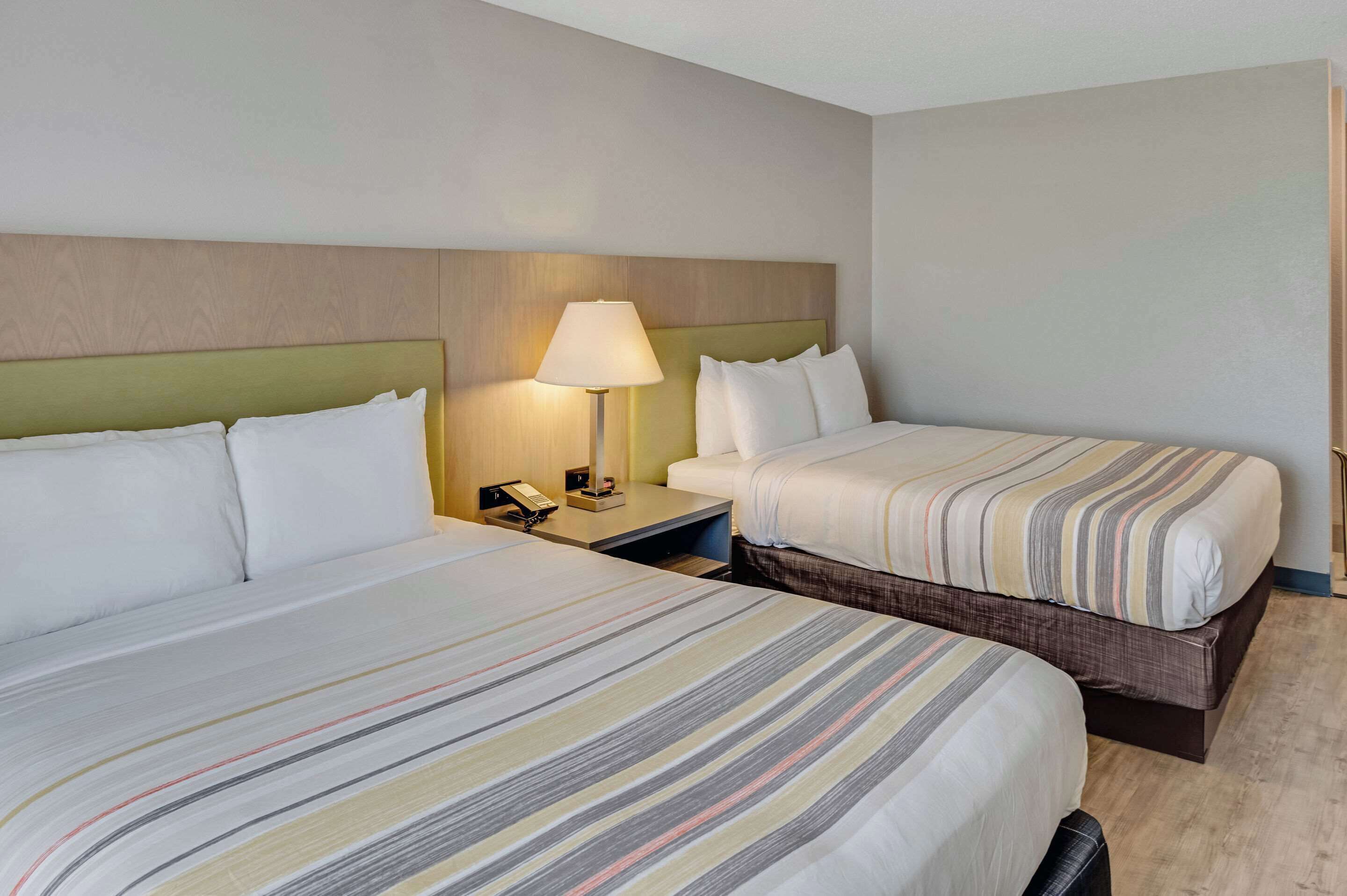 A hotel room with two beds, a nightstand with a lamp, and a wooden headboard.