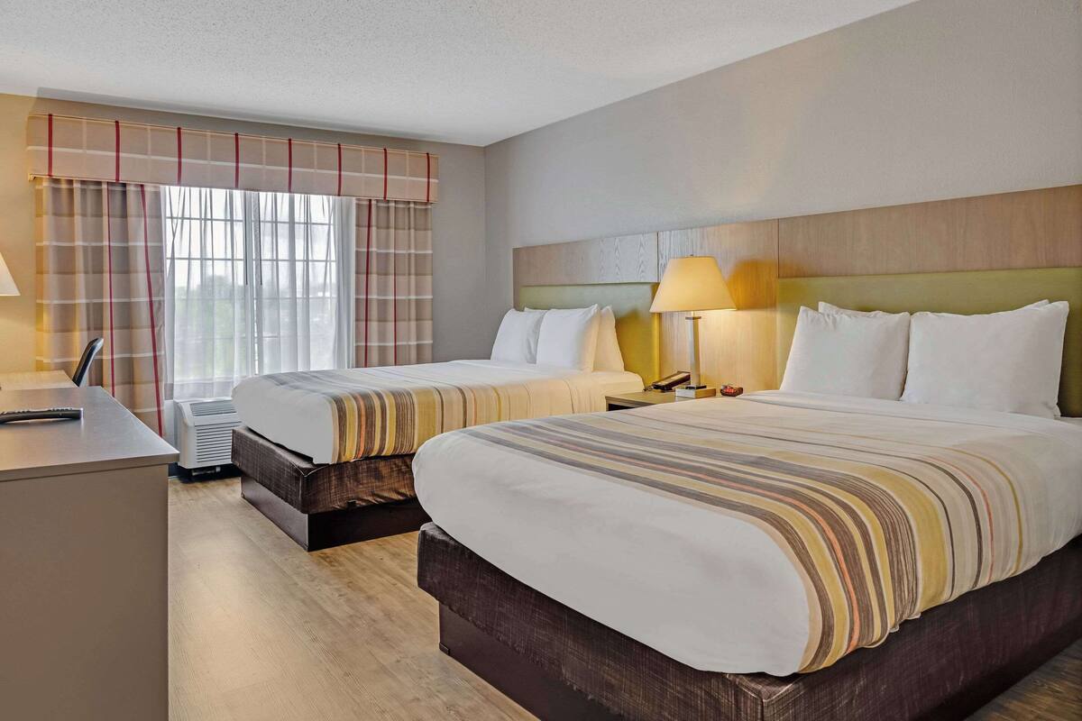 A hotel room with two beds, a desk, and a nightstand with lamps.