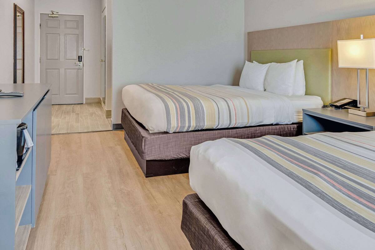 A hotel room with two beds, a desk, a chair, a lamp, and a door.