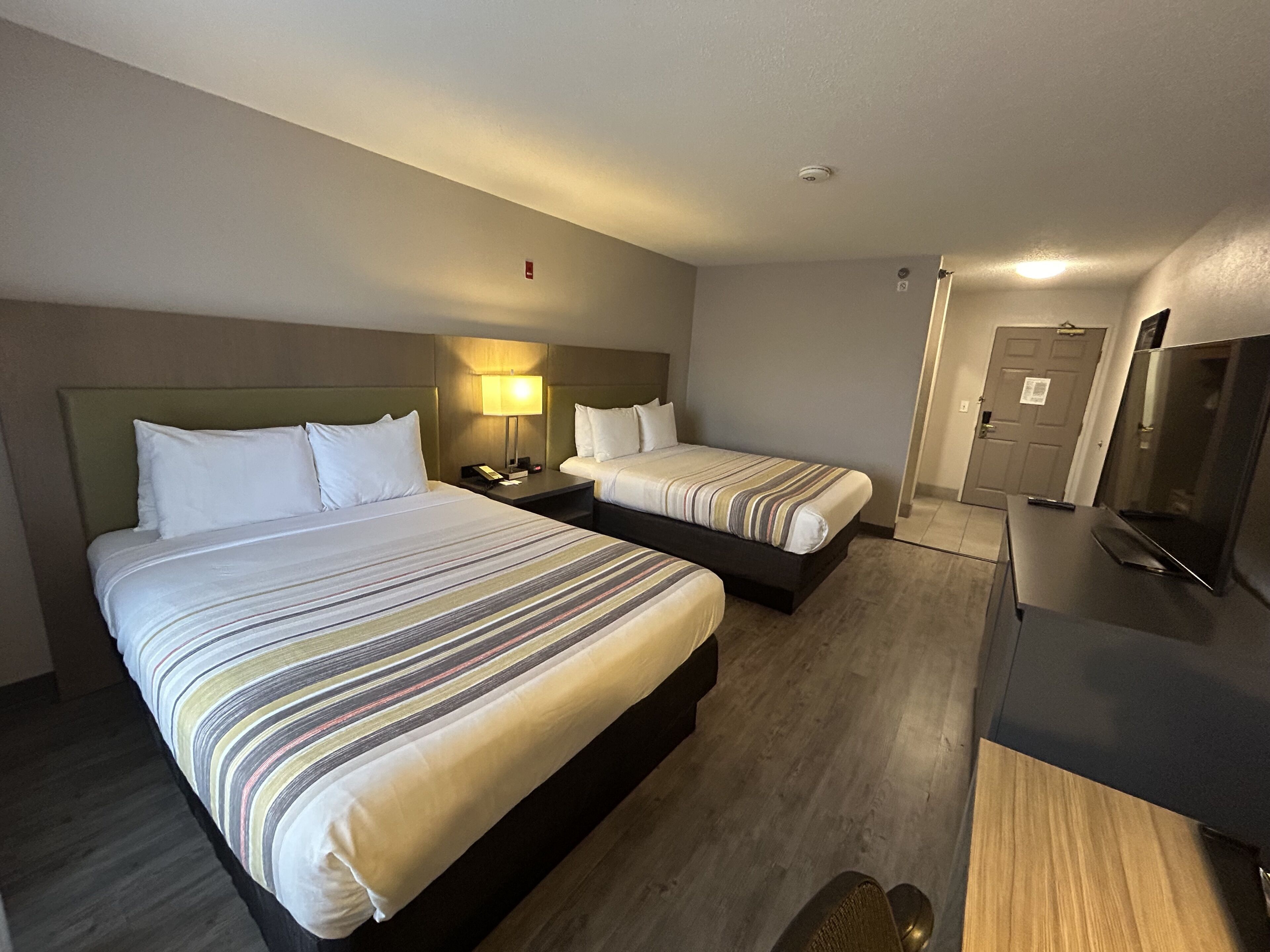 A hotel room with two beds, a desk, a TV, and a door.