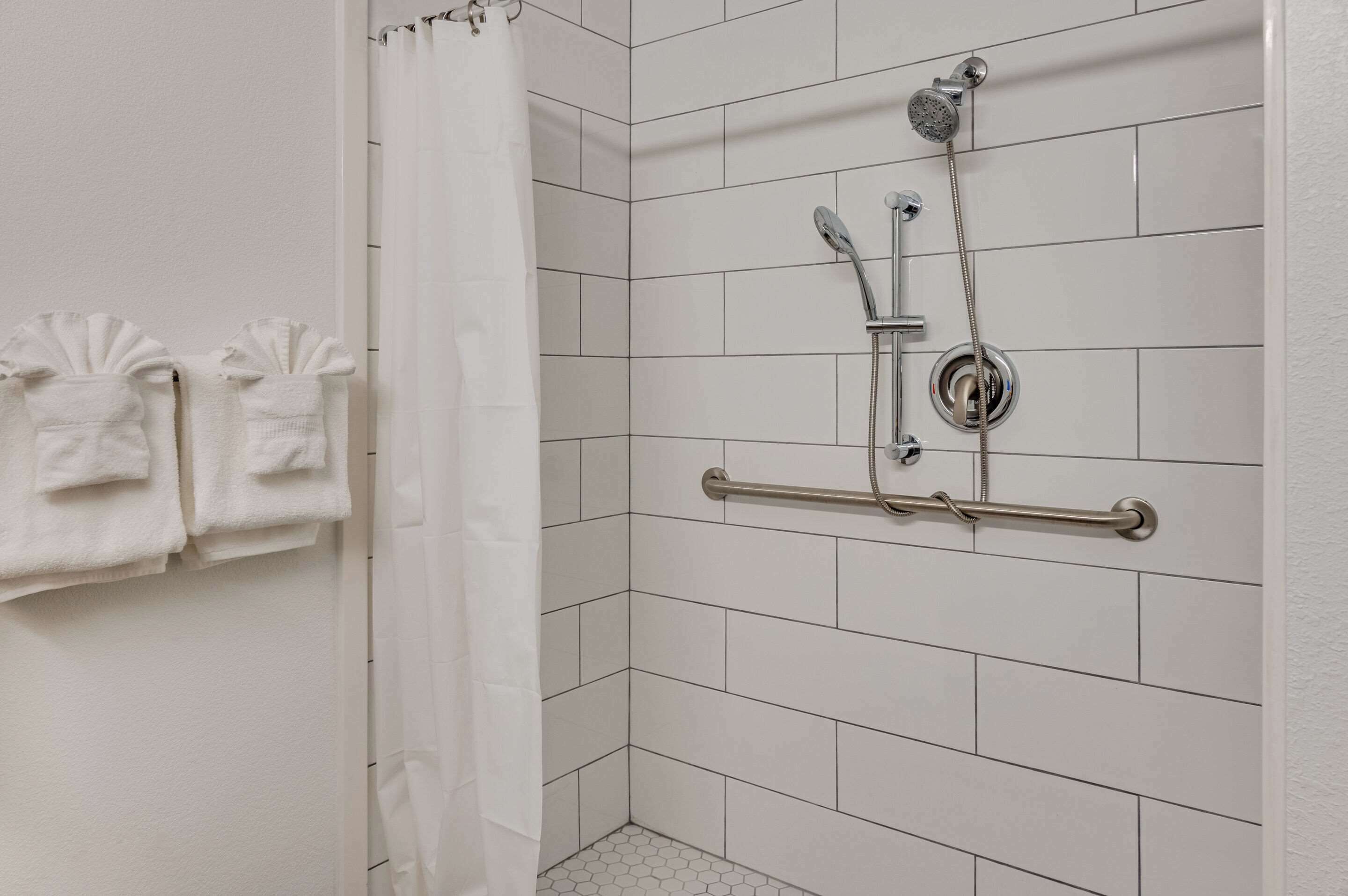 A shower area with white tiles, a showerhead, a handheld showerhead, and a grab bar.
