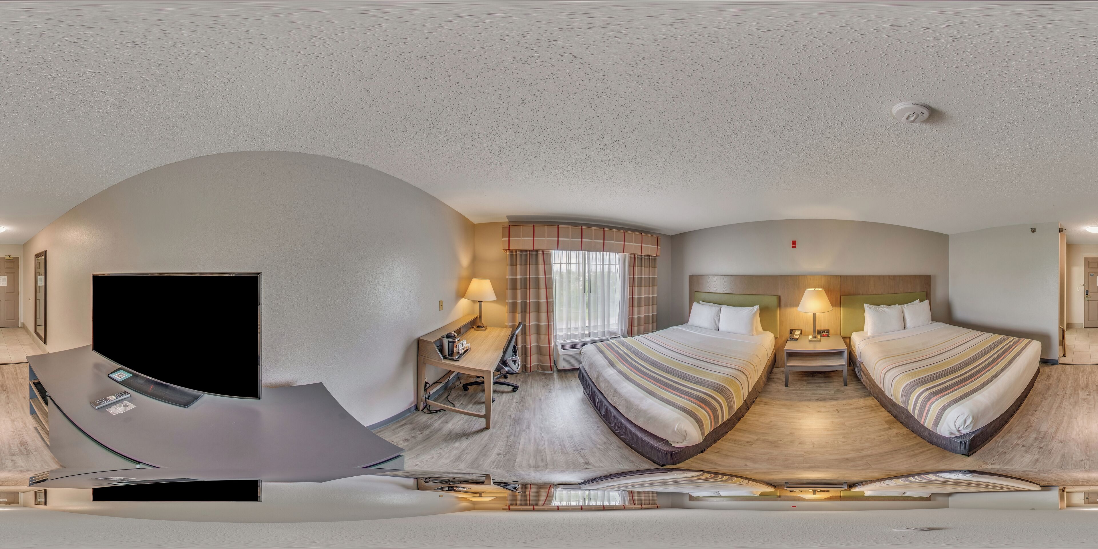 A hotel room with a curved ceiling, a desk with a flat-screen TV, two beds with striped bedding, and a window with curtains.