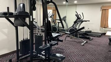 A gym with various exercise equipment, including a bench, a squat rack, and treadmills.