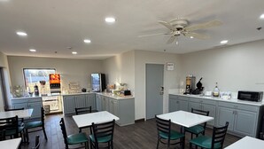 A modern kitchen with white cabinets, a central island, and a dining area with white tables and green chairs. - Quality Inn Jacksonville near Little Rock Air Force Base (Jacksonville)