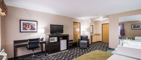 Habitación de hotel con cama, escritorio con computadora, televisor, microondas, sillón y baño con lavamanos y bañera.
