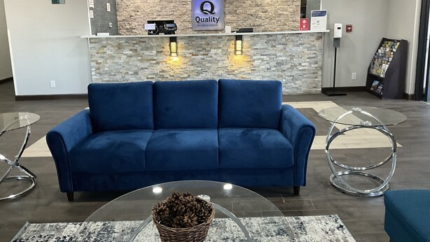 A reception area with a blue sofa, a glass table with a basket, and a stone wall with a 'Quality by Choice Hotels' sign. - Quality Inn Jacksonville near Little Rock Air Force Base (Jacksonville)
