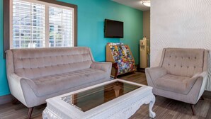 A living room with a beige sofa, a matching armchair, a glass coffee table, a wall-mounted TV, and a bulletin board. - Quality Inn Near Hollywood Walk of Fame (Los Angeles)