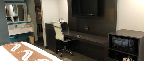 Une chambre d’hôtel comprenant un lit, un bureau avec une chaise, un téléviseur à écran plat, un four à micro-ondes et un petit placard.