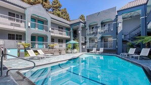 A swimming pool with lounge chairs and a sofa, surrounded by a building with balconies and a tiled roof. - Quality Inn Near Hollywood Walk of Fame (Los Angeles)