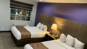 A hotel room with two beds, a window with blinds, a bedside table with a lamp, and a wall-mounted air conditioner. - Quality Inn Near Hollywood Walk of Fame (Los Angeles)