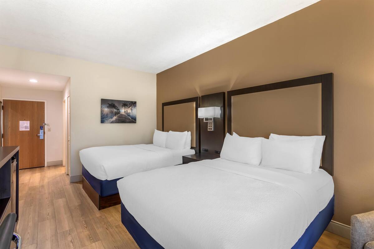 A hotel room with two beds, a desk, and a painting on the wall.