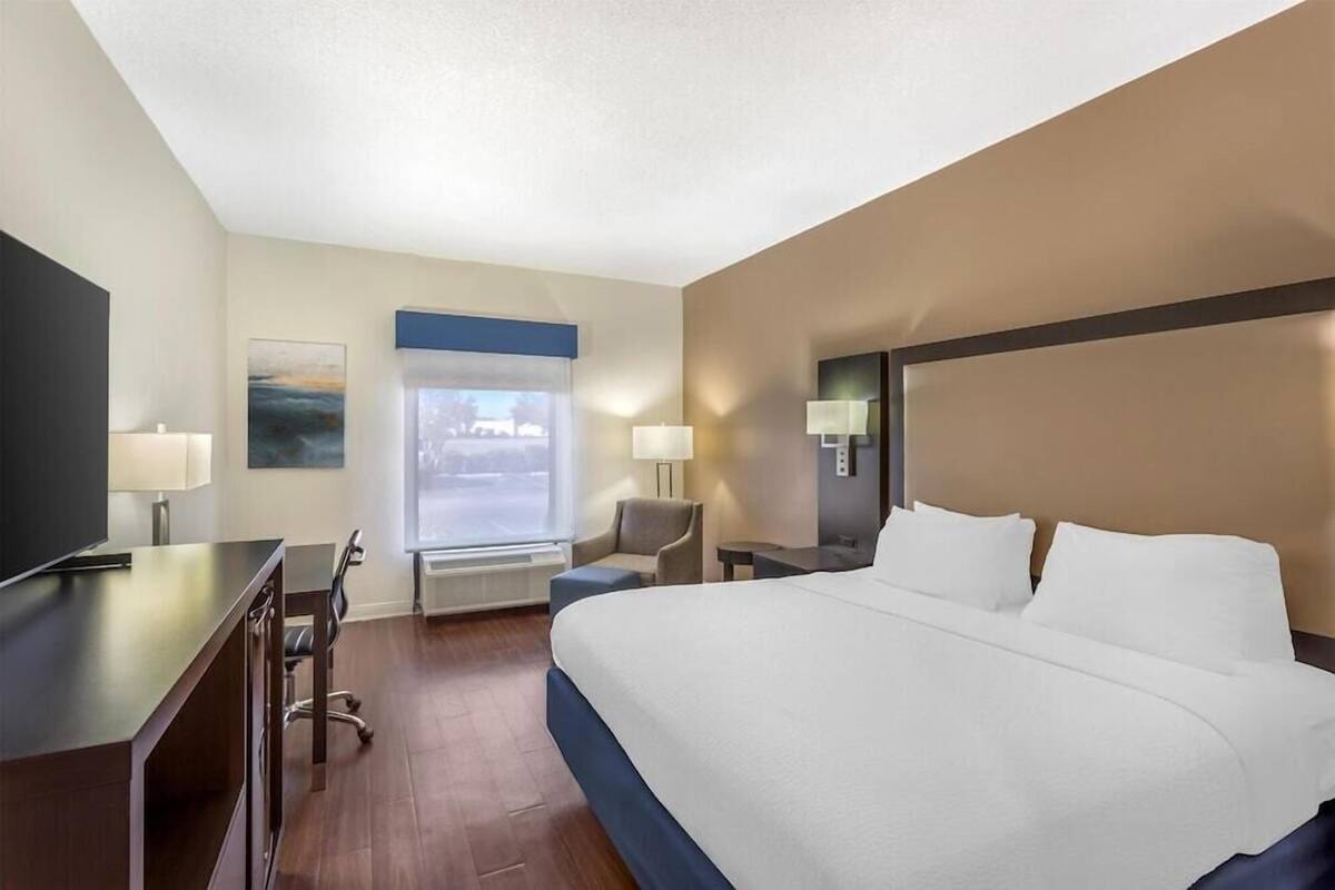 A hotel room with a large bed, a desk, a chair, a TV, and a window with a view.