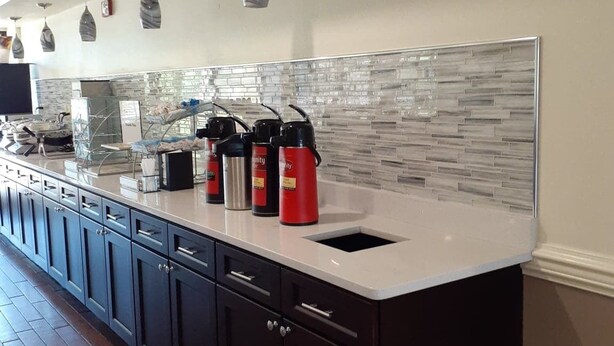 A modern kitchen with a white countertop, dark cabinets, and a glass backsplash. - Best Western Plus Madison (Madison)
