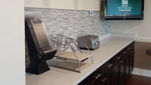 A modern kitchen with a built-in microwave, toaster, and a coffee machine. A flat-screen TV mounted on the wall displays a news channel. - Best Western Plus Madison (Madison)