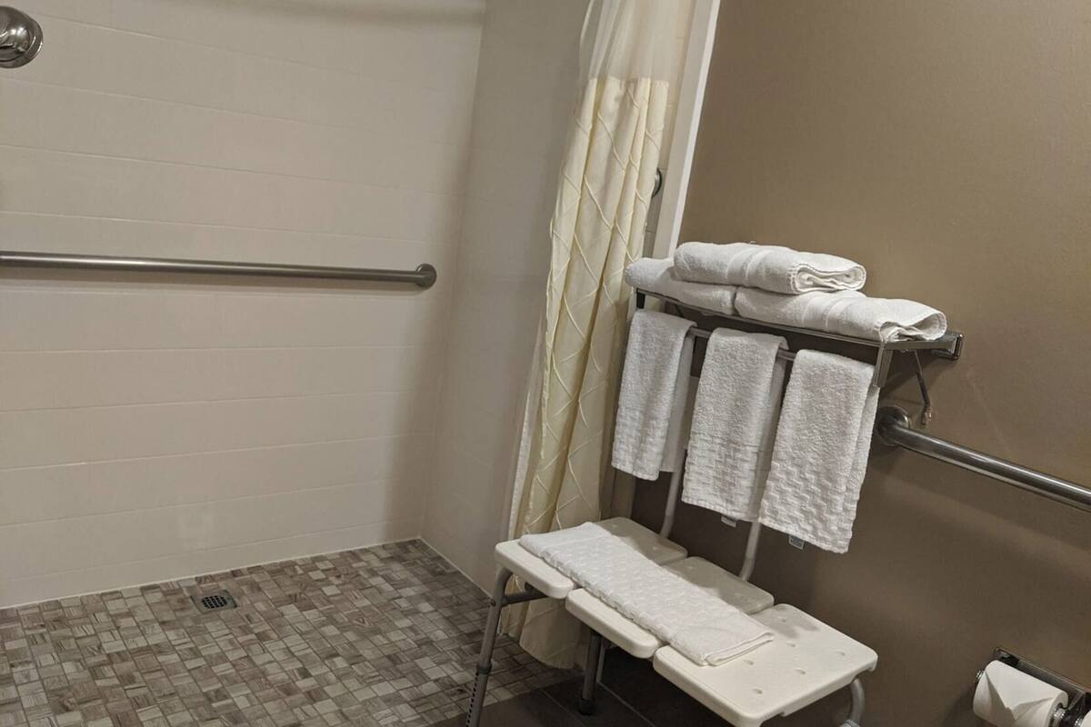 A bathroom with a shower, a bench, a towel rack, and a toilet paper holder.