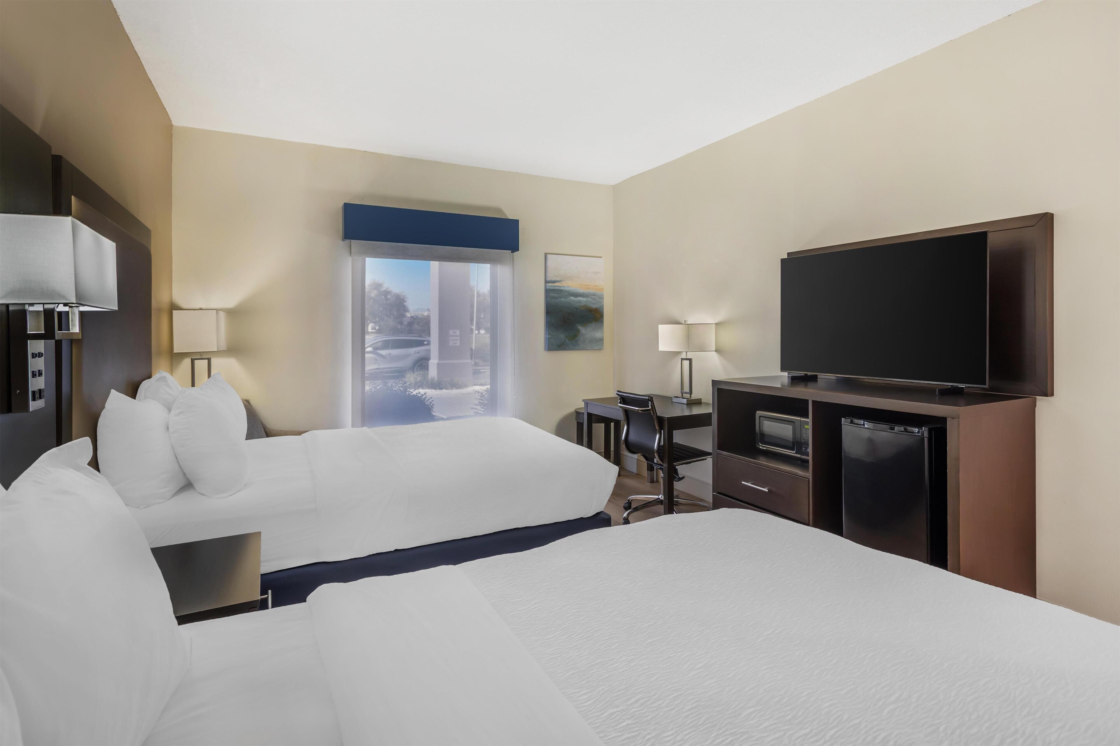 Una habitación de hotel con dos camas, un escritorio, un televisor y un minibar.