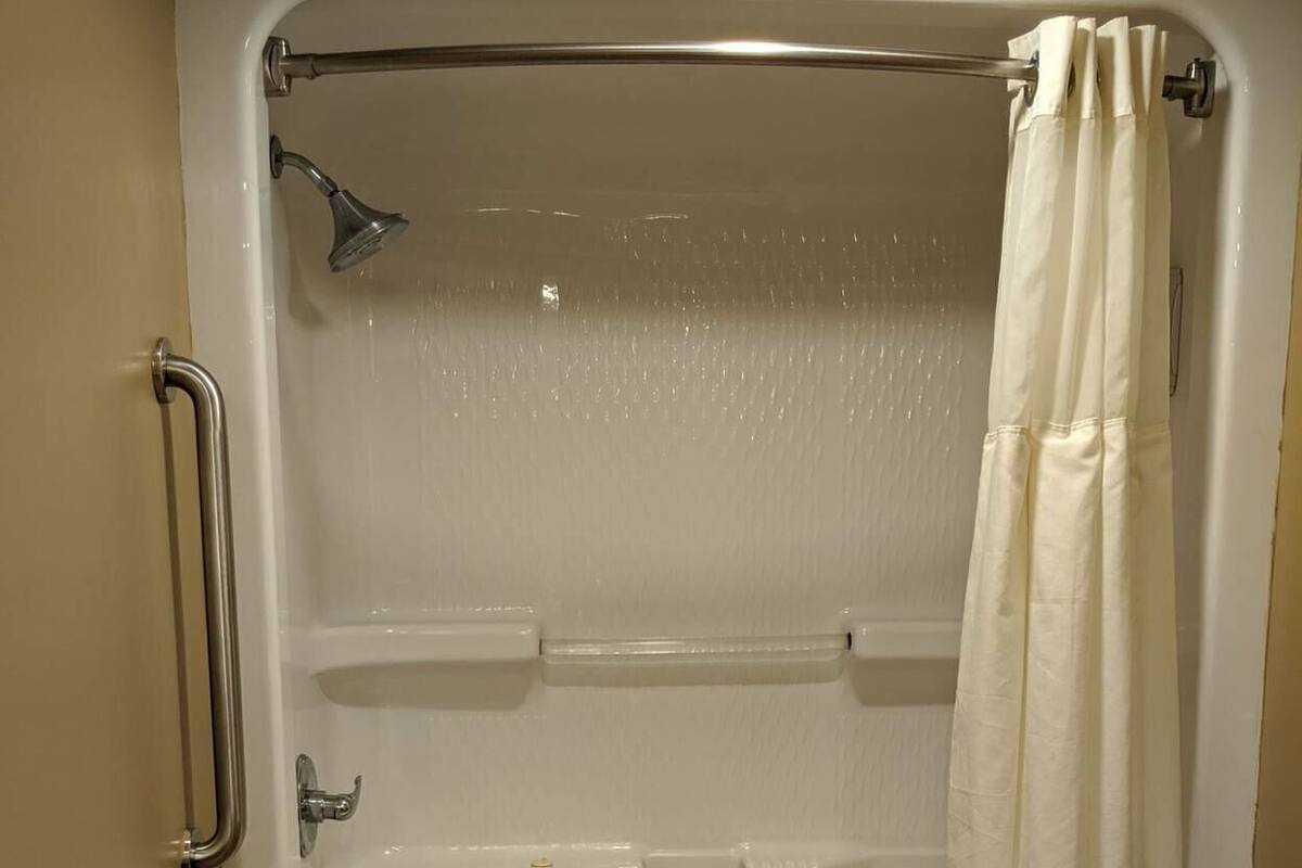 A standard bathtub with a showerhead, grab bars, and a towel rack.