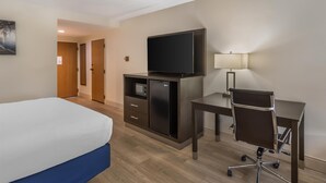 A hotel room with a bed, a desk, a chair, a TV, a lamp, and a minibar. - Best Western Plus Madison (Madison)