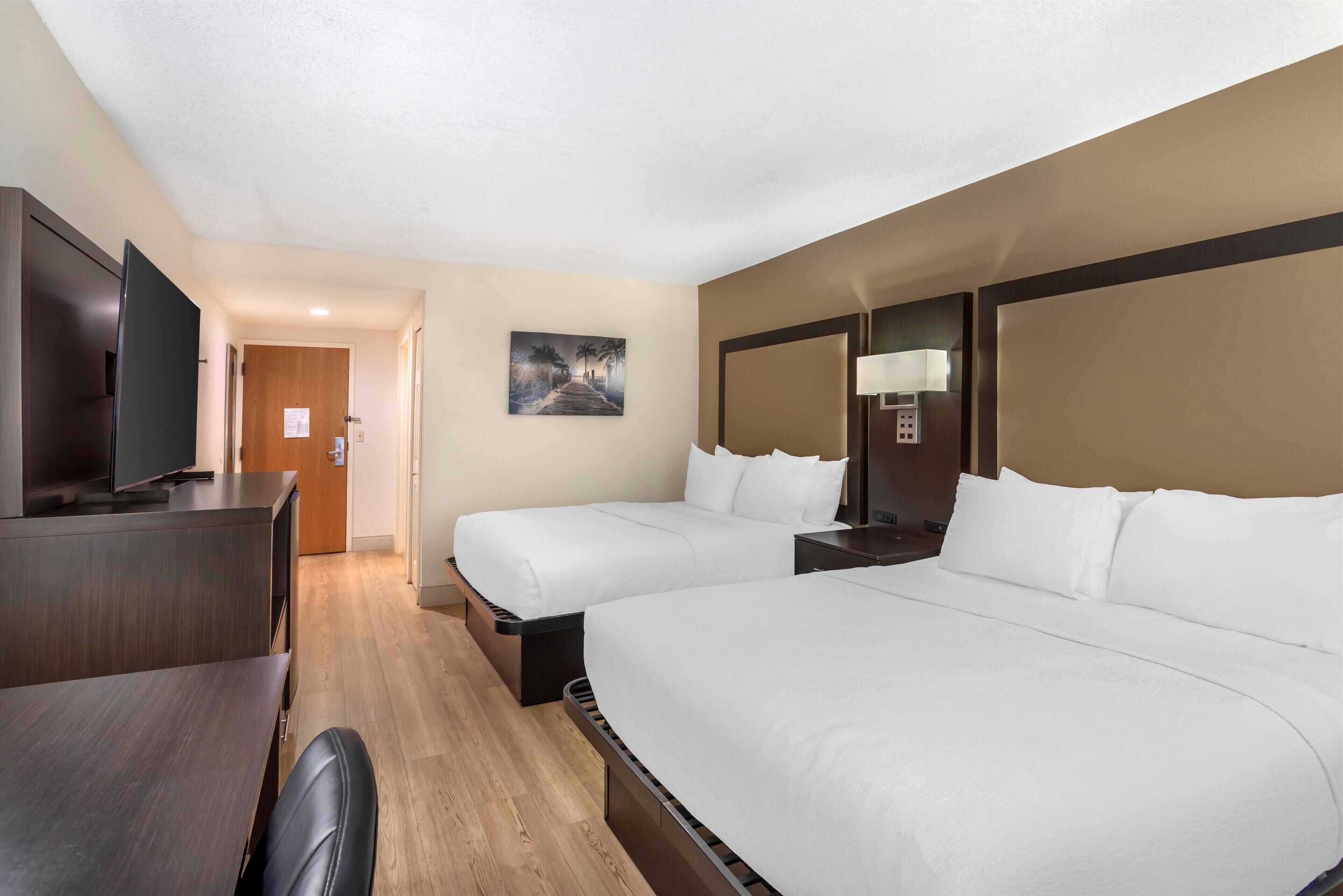 A hotel room with two beds, a desk, a TV, and a painting on the wall.