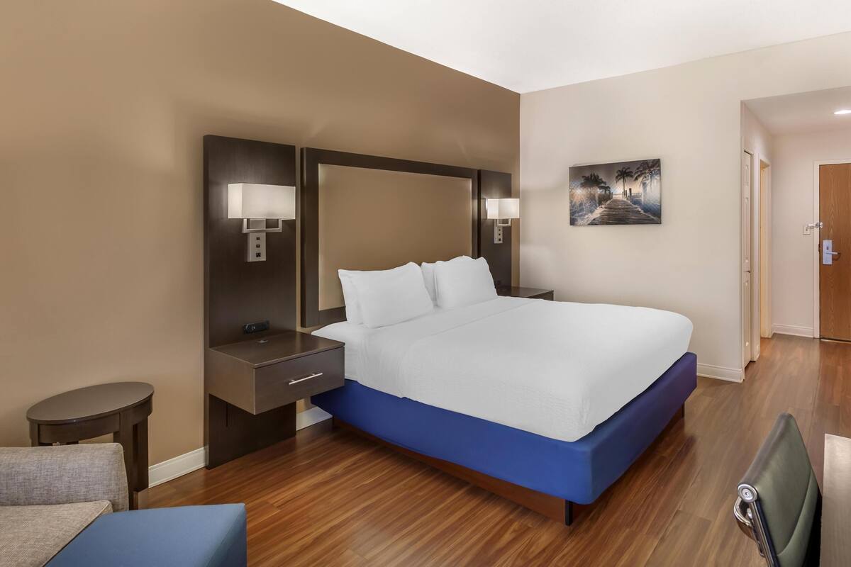 A hotel room with a large bed, a bedside table, a chair, and a painting on the wall.