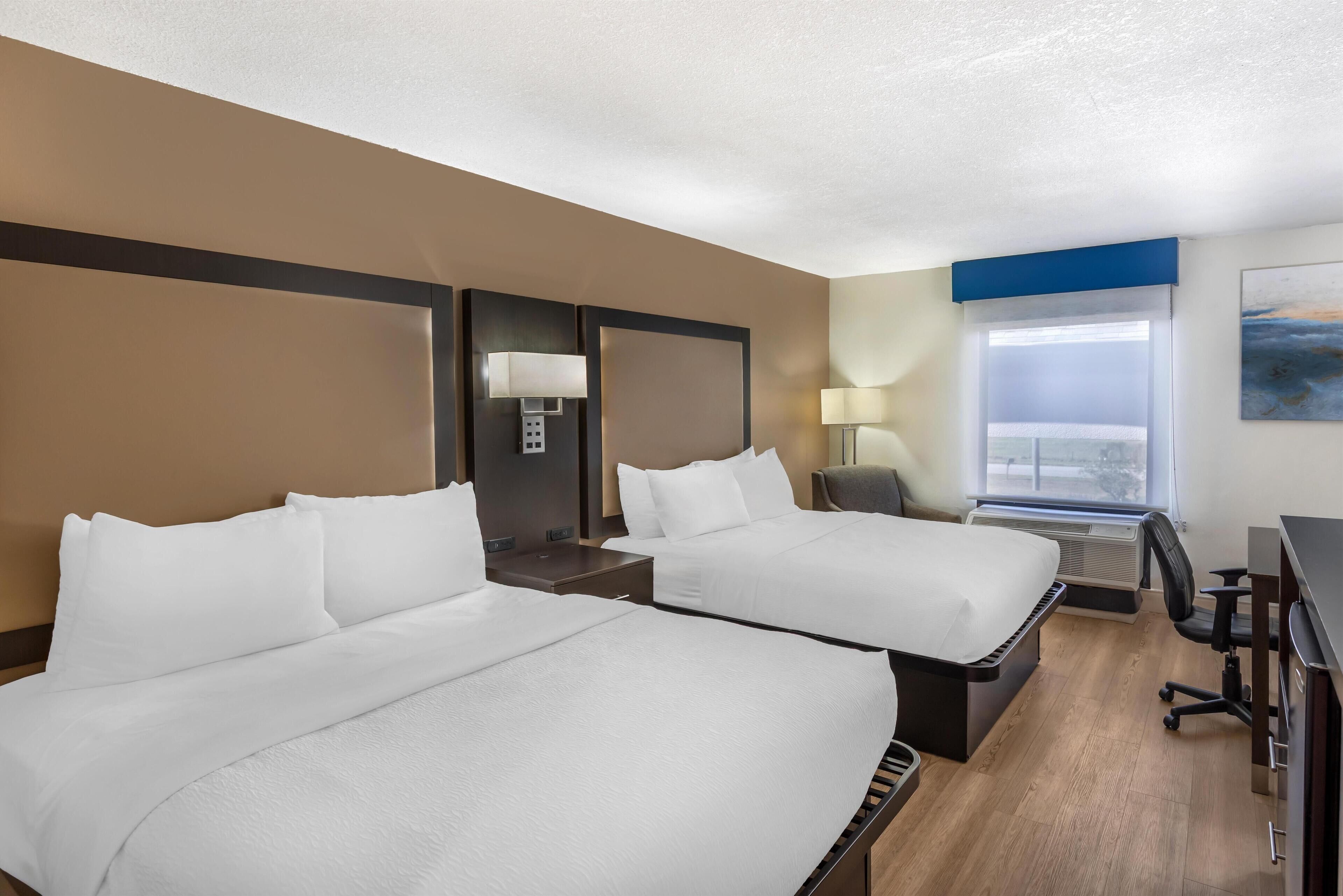 A hotel room with two beds, a desk, a chair, and a large window.