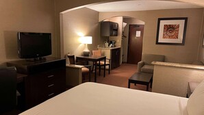 A hotel room with a bed, a TV, a desk with a lamp, a chair, a sofa, and a kitchenette. - Country Inn & Suites by Radisson, Garden City, KS (Garden City)