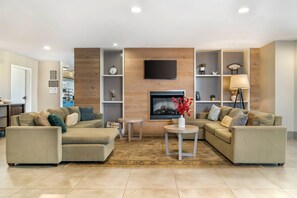 A living room with two sofas, a coffee table, a TV mounted on a wooden wall, and shelves with decorative items. - Country Inn & Suites by Radisson, Frederick, MD (Frederick)
