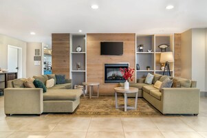 Sala de estar con dos sofás, una mesa de centro, un televisor montado en una pared de madera y estantes con objetos decorativos.