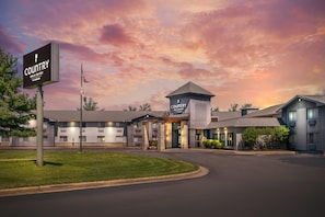Ein Country Inn & Suites Hotel mit modernem Design, einem zentralen Turm und einem gepflegten Rasen.