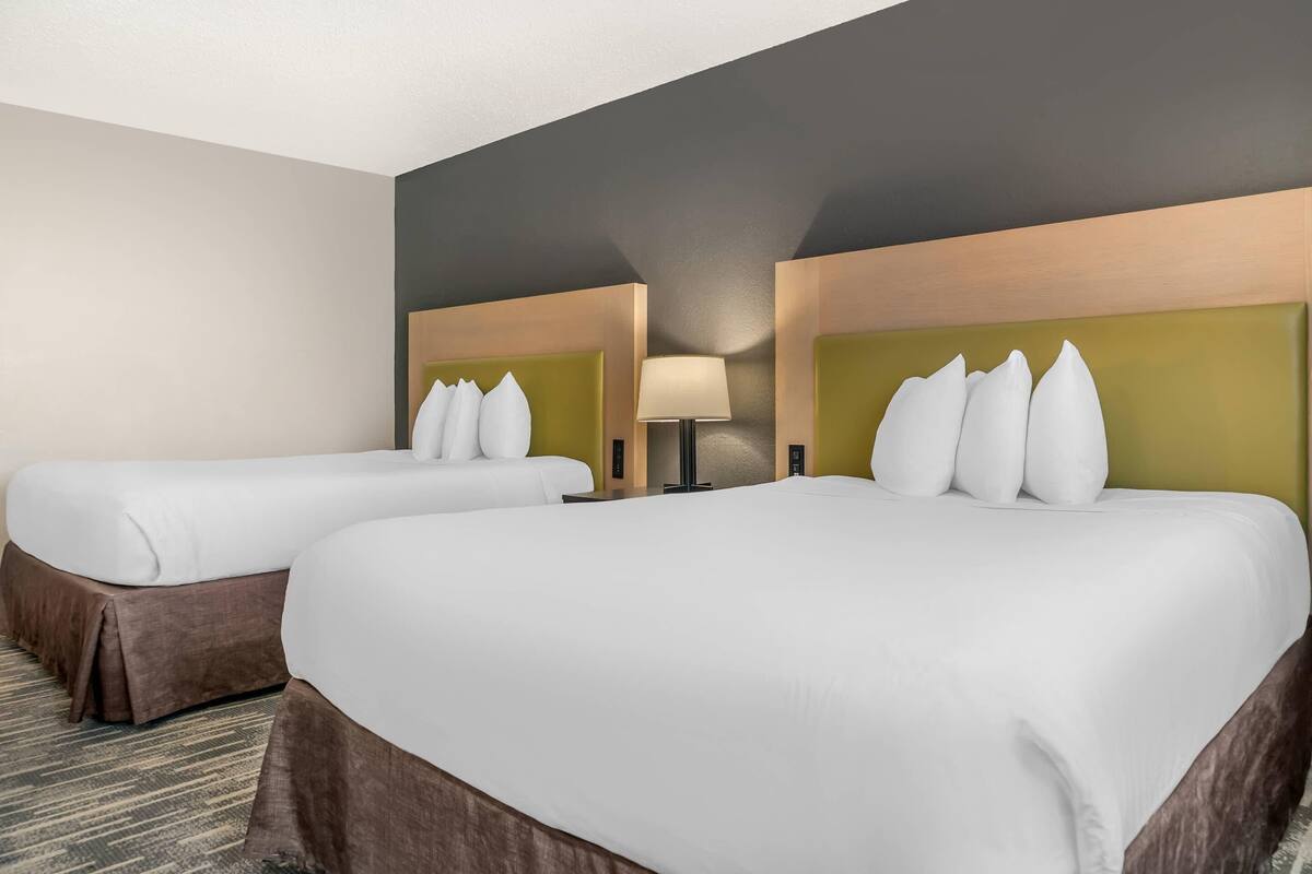 A hotel room with two beds, a large mirror, and a lamp.