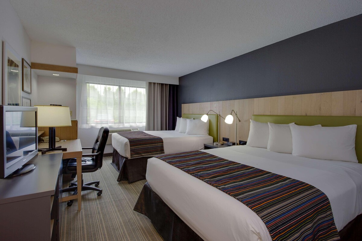 A hotel room with two beds, a desk with a computer, a TV, and a window with curtains.