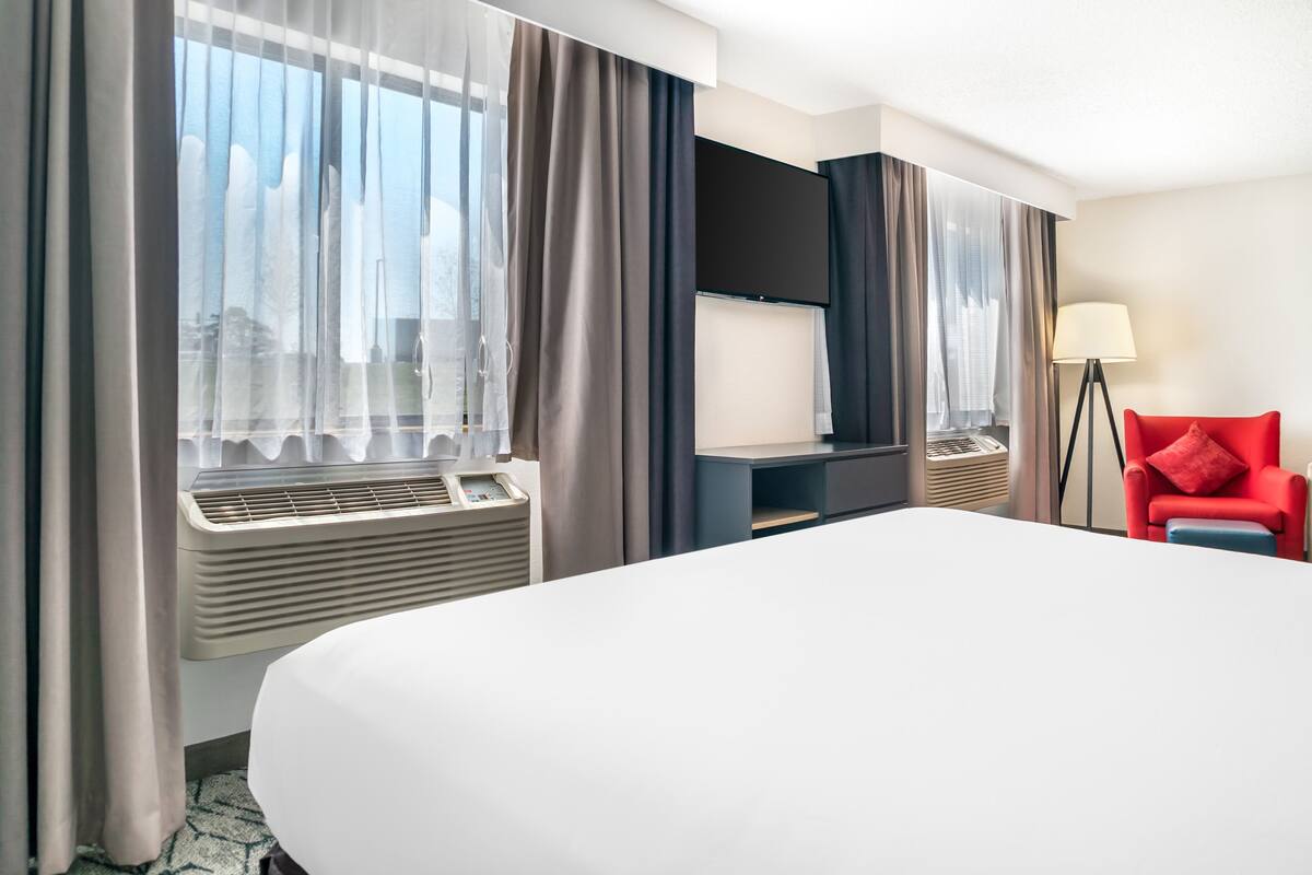 A hotel room with a large bed, a flat-screen TV, a desk, and a red chair.