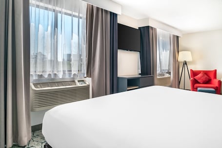 A hotel room with a large bed, a flat-screen TV, a desk, and a red chair.