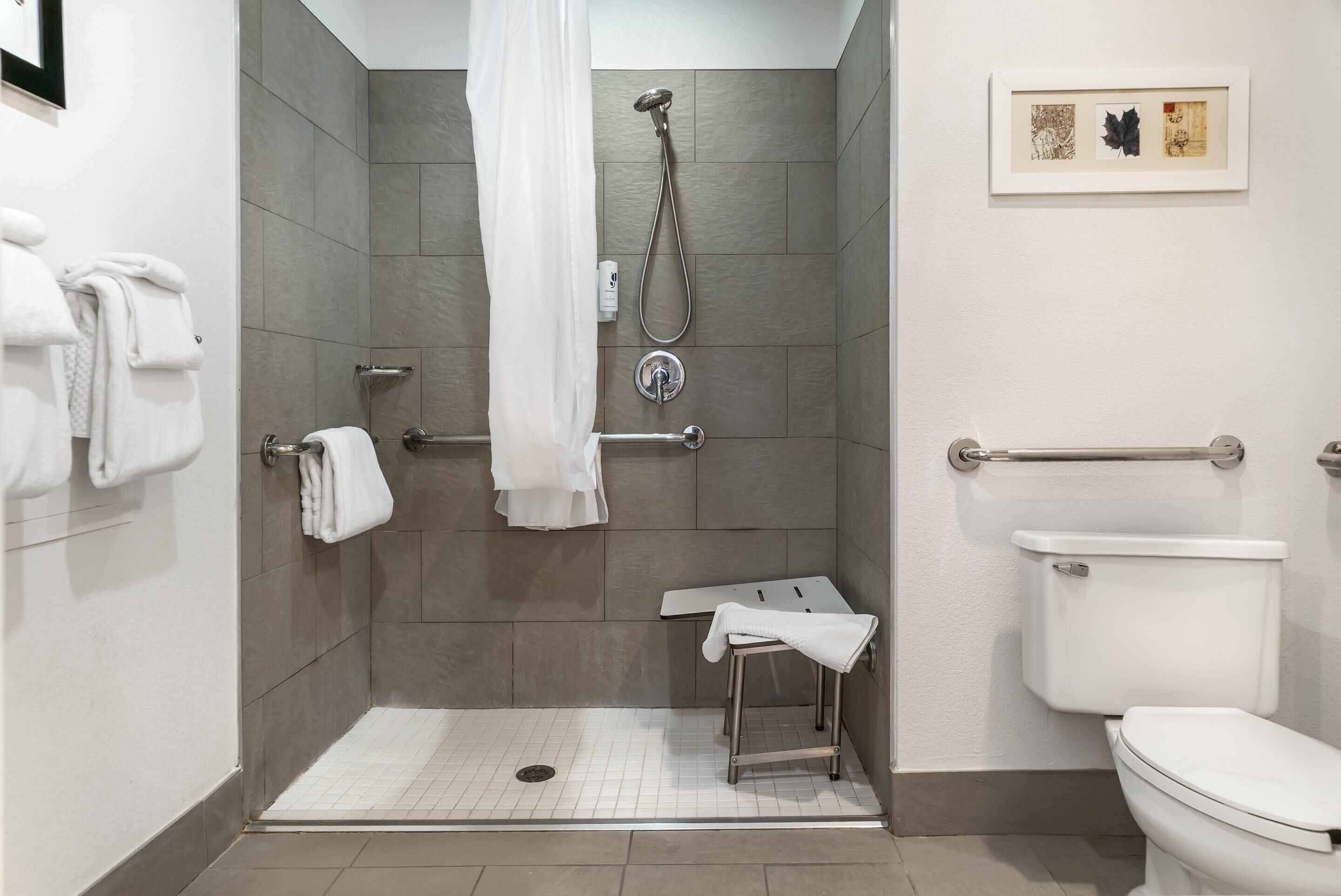 A bathroom with a shower, toilet, and a small table with a towel.