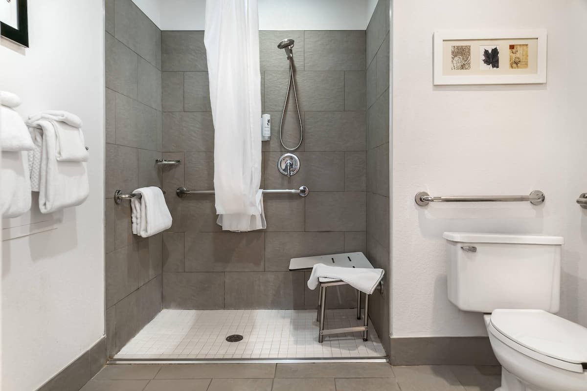 A bathroom with a shower, toilet, and a small table with a towel.