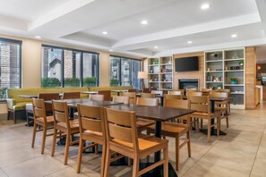 A modern dining area with wooden tables and chairs, a sofa, and a television on a wall. - Country Inn & Suites by Radisson, Frederick, MD (Frederick)