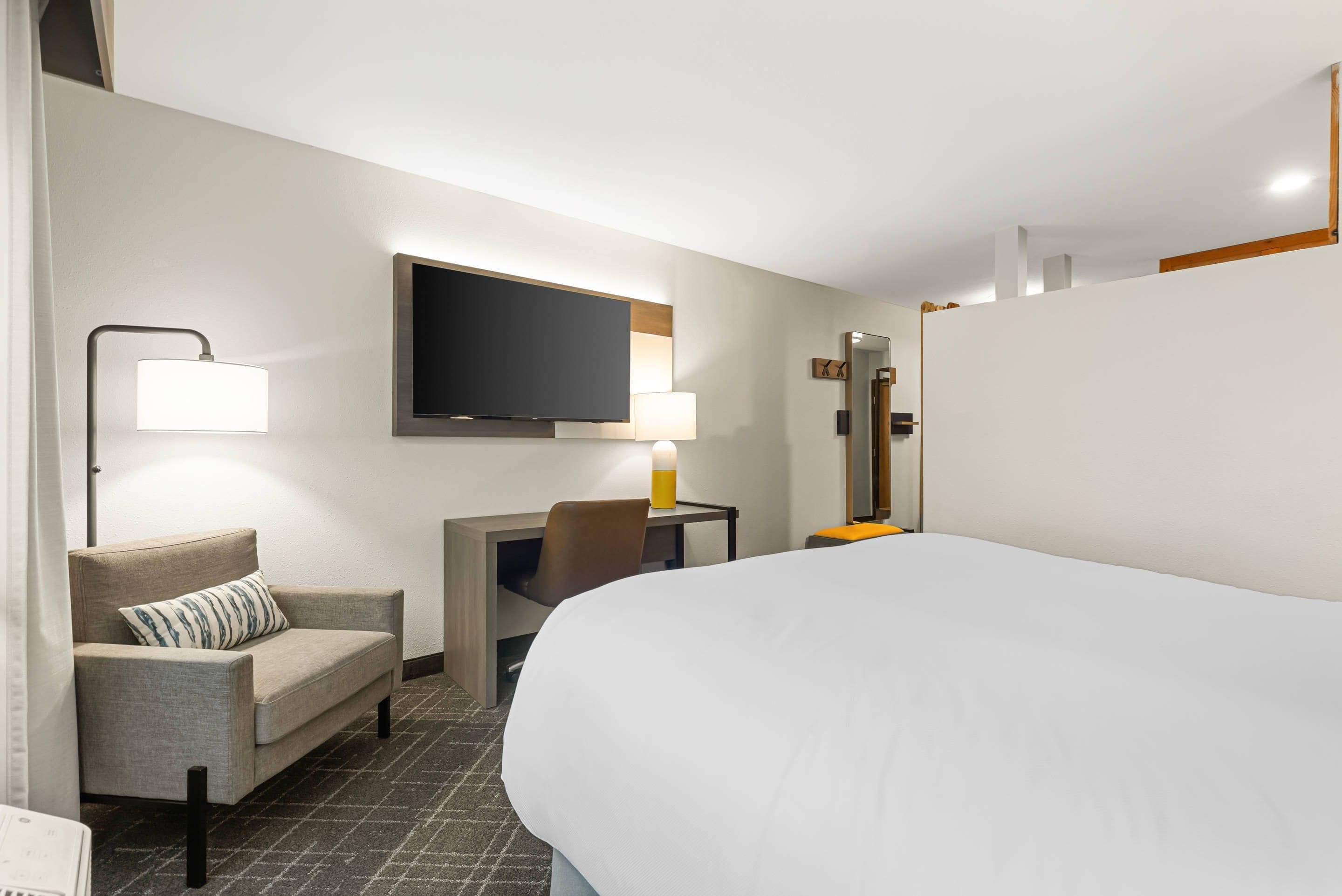A hotel room with a bed, a desk, a chair, a television, and a lamp.